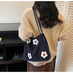 Détail du sac fourre-tout en tricot bleu marine avec broderies florales blanches et lanières