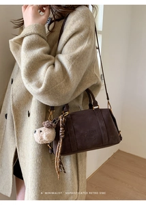 Detail of retro coffee brown suede Boston bag with logo embossing and plush charm