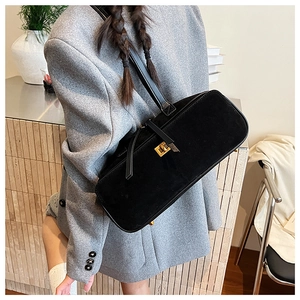 Detail of a black velvet baguette bag with a vintage gold twist lock worn as a shoulder bag