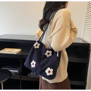 Détail d'un sac cabas en tricot bleu marine avec broderie de marguerites et lanières en cuir
