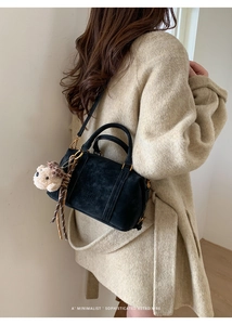 Detail of black Boston bag with SKERT PARIS logo and cute beige teddy bear pendant