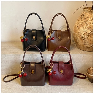 Detail of four retro bucket bags in black, brown, and burgundy with cherry pendants