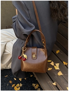 Macro shot of a dark brown retro leather bucket bag with a cherry pendant on a wooden bench