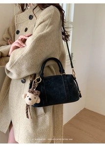 Detail of black retro suede handbag with plush bear charm and embossed branding