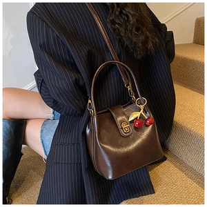 Detail of dark brown oil wax leather bucket bag with gold twist lock and cherry charm