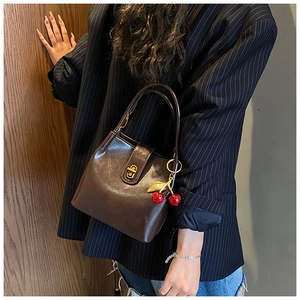 Detail of dark brown glossy bucket bag with golden twist lock and cherry charm accessory