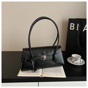Detail view of black glossy leather Boston bag with silver shield buckle and long handles