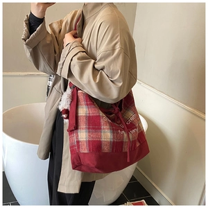 Detail of red plaid tote bag featuring fuzzy ball charm and creative text print decoration