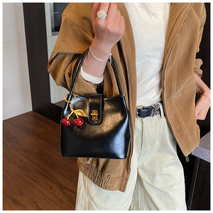 Fashionable black bucket bag with a red cherry charm shown on model in a studio setting