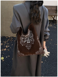 Detail of bohemian white embroidery on dark brown suede tote bag carried on shoulder