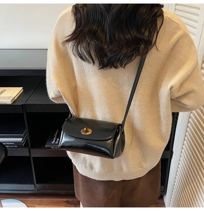 Détail d'un sac bandoulière noir avec fermoir doré rotatif porté sur un pull beige élégant