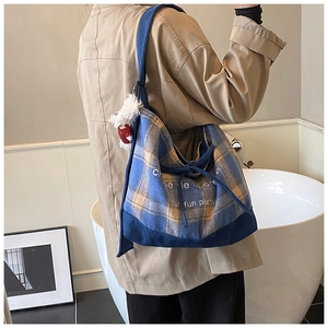 Detail of blue and yellow plaid canvas tote bag with artistic text and plush doll pendant