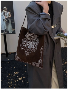Detail of white embroidery patterns on dark brown suede tote bag in autumn setting