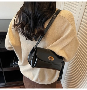 Détail d'un sac bandoulière noir brillant avec fermoir métal porté par un mannequin