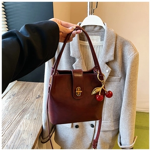 Detail of burgundy bucket bag with golden twist lock and cherry charm accessory