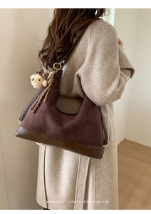 Detail of vintage brown suede tote bag with logo embossing and cute bear charm pendant