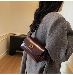 Détail du sac sous l'aisselle en cuir verni bordeaux avec fermoir ovale doré