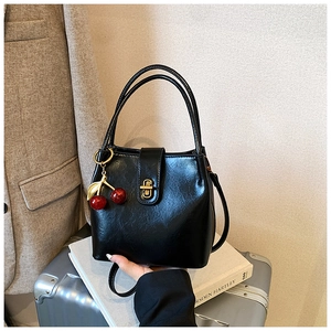 Detail of black glossy bucket bag with golden twist lock and cherry pendant charm