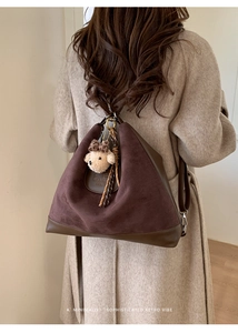 Detail of vintage brown suede tote bag with metal ring buckle and bear charm on wool coat