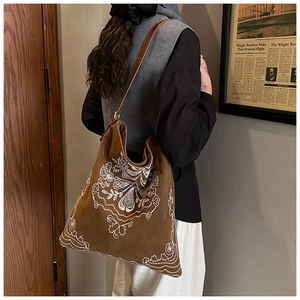 Detail shot of white floral embroidery on a brown suede vintage tote bag being worn