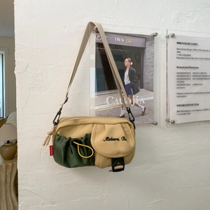 Detail der khakifarbenen Umhängetasche mit grüner Kordelzugtasche und schwarzen Beschlägen