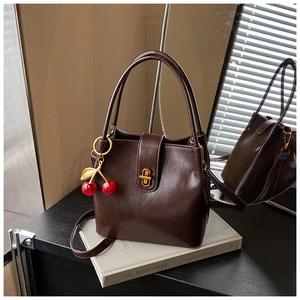 Detail of dark coffee leather bucket bag with gold twist lock and cherry charm on books