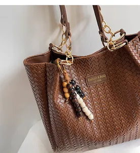 Détails de la texture du sac cabas tressé marron avec pompon perlé et bandoulière chaîne