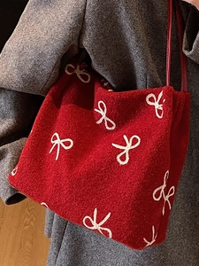 Sac fourre-tout en feutre rouge avec broderies nœuds porté sur un manteau gris par un mannequin