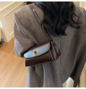 Sac bandoulière en cuir marron avec fermoir doré porté sur une veste en laine grise