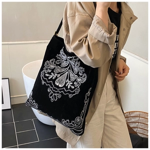 Detailed white ethnic embroidery on a black suede tote bag shown on a model