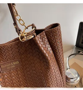 Gros plan détaillé de la texture en cuir tressé d'un sac cabas marron avec chaîne dorée
