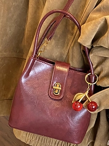 Vintage burgundy leather bucket bag with gold lock and cherry charm over a brown coat