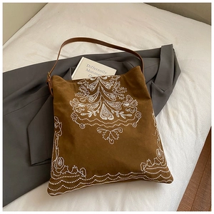 Detailed close-up of ethnic embroidery on dark brown suede tote bag in a casual setting