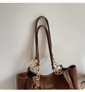 Détail du cabas tressé marron avec bandoulière en chaîne dorée et plaque logo en métal