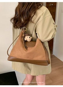 Close-up of brown suede tote with leather bottom, logo embossing, and plush charm
