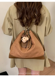 Detail of vintage brown suede tote bag with bear charm and leather stitching on model back