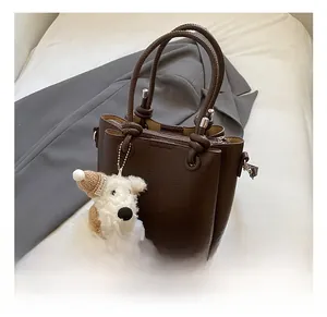 Close-up of deep brown lychee grain leather tote with knotted handle and plush dog charm