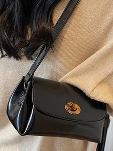 Sac bandoulière chic en cuir brillant noir avec fermoir rotatif doré sur modèle