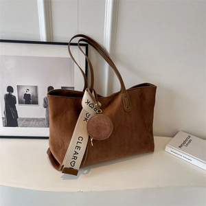 Detailed close-up of brown suede tote bag with quilted texture and wide logo strap