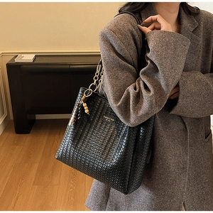 Gros plan du sac cabas tissé noir avec bandoulière en chaîne dorée et accessoires