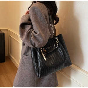 Détail du sac cabas tissé noir avec bandoulière chaîne sur un manteau en laine