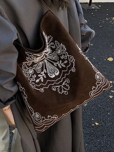 Ethnic embroidered brown faux suede tote bag shown on shoulder in outdoor setting