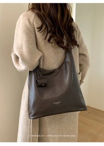 Grand sac cabas en cuir marron avec un charme cylindrique assorti porté par un mannequin