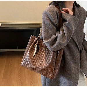 Détail d'un sac cabas tressé marron avec breloque perlée et bandoulière chaîne dorée