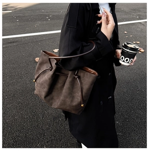 Detail of deep brown textured leather tote bag with gold bead charms on a street background