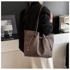 Detail of a large brown matte leather tote bag with a gold bead drawstring closure