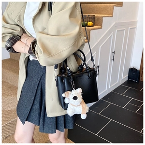 Detail of black lychee grain leather bucket bag with a cute white puppy plush charm