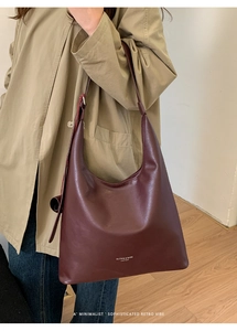 Sac hobo minimaliste en cuir bordeaux porté par un mannequin dans un intérieur moderne
