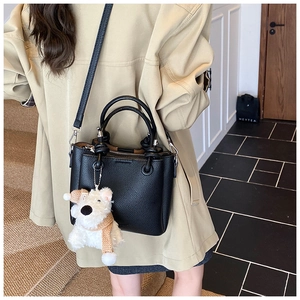 Detail of black lychee grain leather tote bag featuring a cute white teddy bear charm