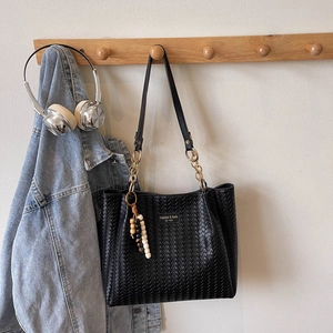 Détail d'un cabas tressé noir avec bandoulière chaîne et pendentif en perles